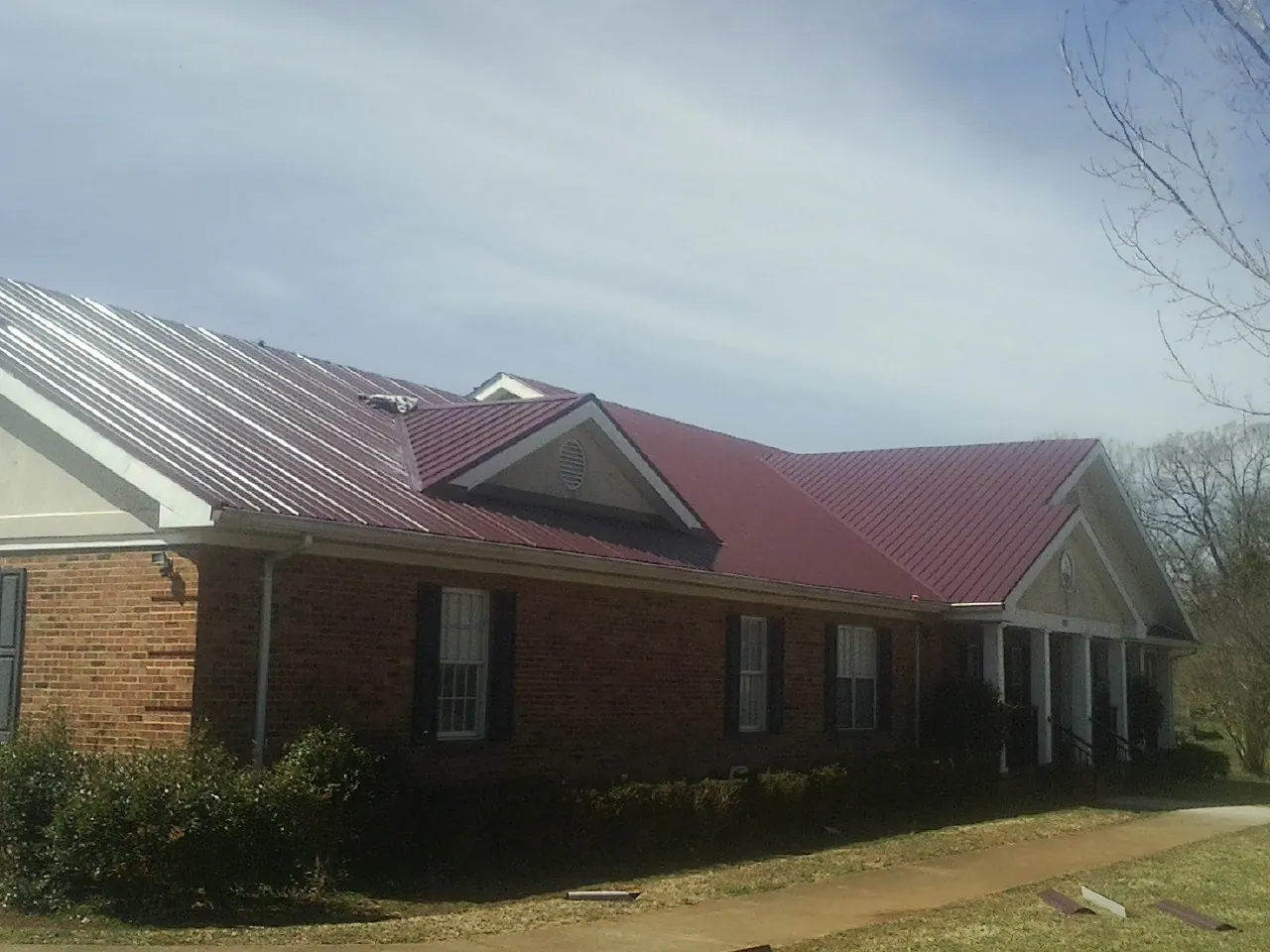 Red metal roof with gabled entries on a long brick building, from a Hail Damage Roof Repair job in Barhamsville