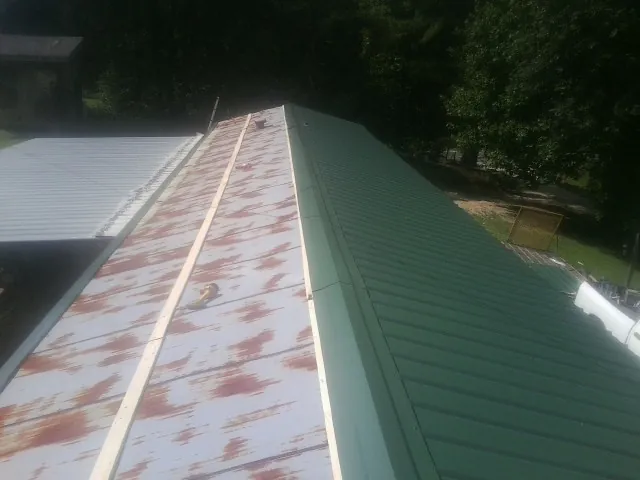 Old rusted panels beside newly installed green metal roofing — Wind Damage Roof Repair by Roofing Brothers in Barhamsville