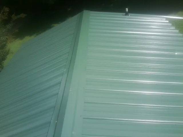 New green metal panels meeting at the ridge of a roof — Flat Roof Repair work by our crew in Barhamsville