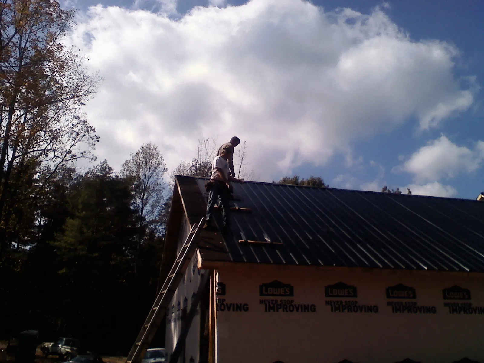 Roofer fastening dark metal panels high against a cloudy sky, from a Roof Inspection job in Barhamsville
