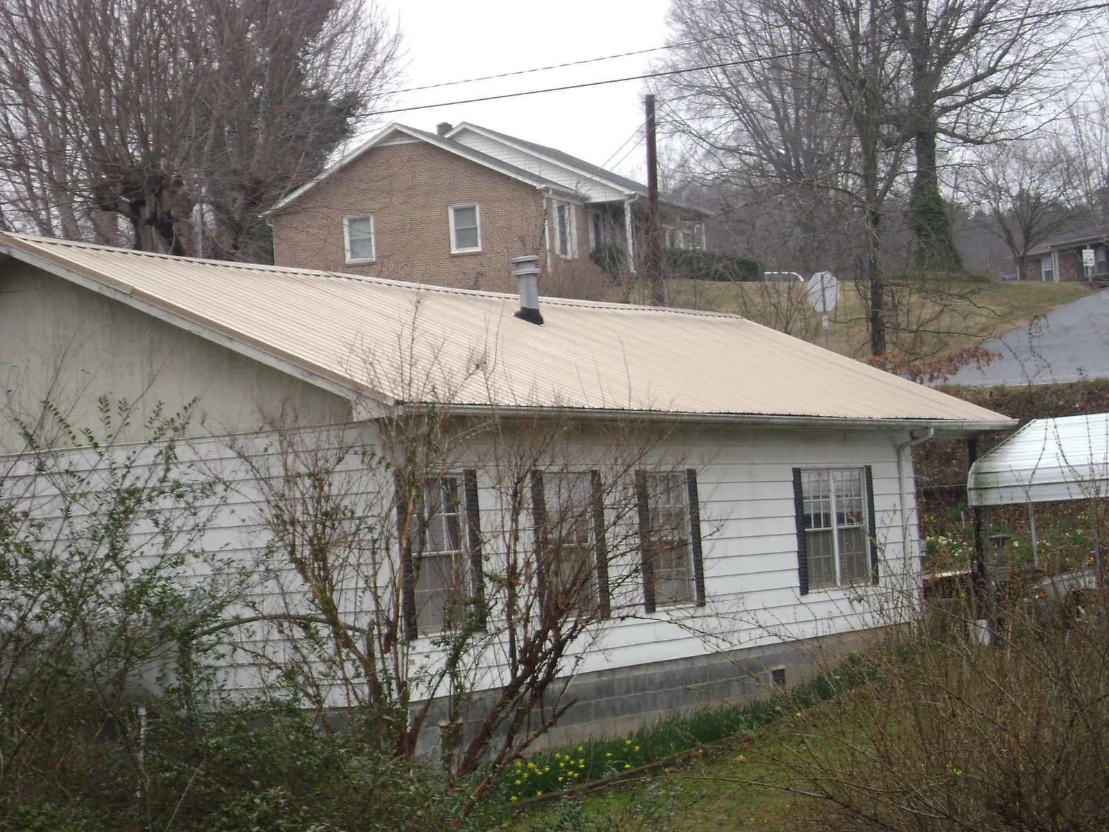 Tan metal roof on a white sided house set into a hillside — Commercial Roofing by Roofing Brothers in Barhamsville